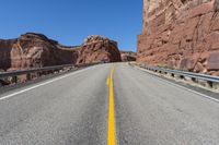 a yellow line on the highway in front of red mountain mountains and a bright blue sky