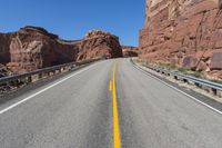 a yellow line on the highway in front of red mountain mountains and a bright blue sky