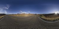 a 360 - fish eye view of an empty road in desert landscape with trees and hills in background