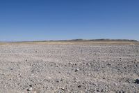 an arid field with no grass in it and dirt around the field and mountains in the distance