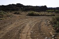 the dirt road is being cleared off by rocks and shrubs in the desert area next to an arch