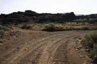 the dirt road is being cleared off by rocks and shrubs in the desert area next to an arch