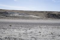 a dirt road is surrounded by some hills and desert like terrain as the vehicle sits on it