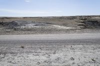 a dirt road is surrounded by some hills and desert like terrain as the vehicle sits on it