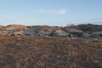 the dirt in this field is covered with sparse vegetation and grass and hills are visible behind the hills