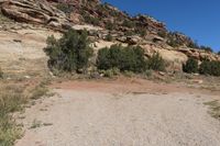 a dirt road leading up to a rock wall in a desert area with a blue sky overhead