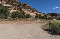 a dirt road leading up to a rock wall in a desert area with a blue sky overhead