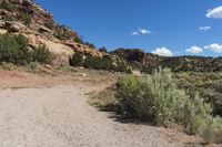 a dirt road leading up to a rock wall in a desert area with a blue sky overhead