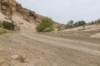 a dirt road with rocks in the background and bushes on each side of it,