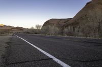 an empty paved road passing through the desert and mountains in winter time during twilight hours