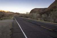 an empty paved road passing through the desert and mountains in winter time during twilight hours