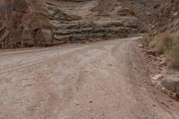 a lone man riding his motorcycle on the side of a dirt road through a gorge