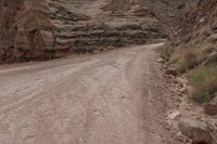 a lone man riding his motorcycle on the side of a dirt road through a gorge