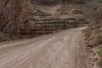 a lone man riding his motorcycle on the side of a dirt road through a gorge