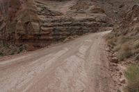 a lone man riding his motorcycle on the side of a dirt road through a gorge