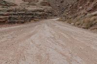 a dirt road going up a steep hill with rocky formations behind it on both sides