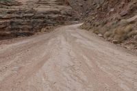 a dirt road going up a steep hill with rocky formations behind it on both sides