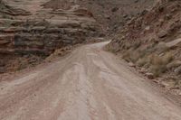 a dirt road going up a steep hill with rocky formations behind it on both sides