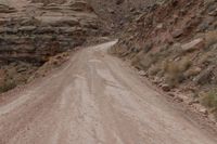 a dirt road going up a steep hill with rocky formations behind it on both sides