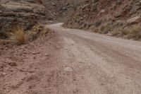 a dirt road going through a canyon by a mountain with no leaves on it, in a desert area