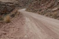 a dirt road going through a canyon by a mountain with no leaves on it, in a desert area