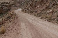 a dirt road going through a canyon by a mountain with no leaves on it, in a desert area