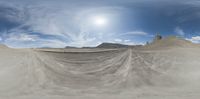 a wide angle shot shows desert like area with mountains in the background and sun behind