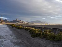 a gravel road in front of a beach covered in snow and mountains in the background