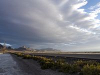 a gravel road in front of a beach covered in snow and mountains in the background