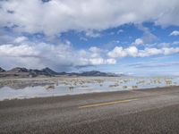 a lonely road stretches out into the desert with mountains in the background and water reflecting the ground