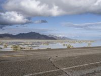 a lonely road stretches out into the desert with mountains in the background and water reflecting the ground