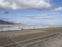 a lonely road stretches out into the desert with mountains in the background and water reflecting the ground