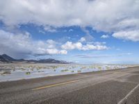 a lonely road stretches out into the desert with mountains in the background and water reflecting the ground