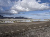 a lonely road stretches out into the desert with mountains in the background and water reflecting the ground