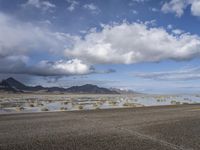 a lonely road stretches out into the desert with mountains in the background and water reflecting the ground