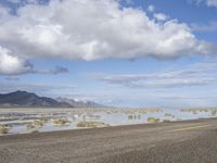 a lonely road stretches out into the desert with mountains in the background and water reflecting the ground