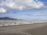 a lonely road stretches out into the desert with mountains in the background and water reflecting the ground