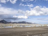 a lonely road stretches out into the desert with mountains in the background and water reflecting the ground