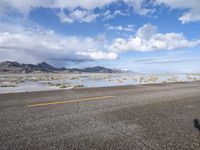 a lonely road stretches out into the desert with mountains in the background and water reflecting the ground