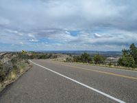 a road near a hill and green trees, clouds and hills in the background,