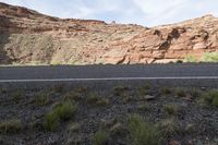 a person riding a motorcycle along a narrow road through rocks and sand cliffs a grassy area on both sides