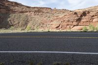 a person riding a motorcycle along a narrow road through rocks and sand cliffs a grassy area on both sides