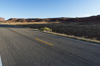 empty desert roadway and mountains, with yellow lines down middle side of street in background