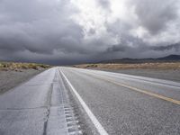 a lone, empty road stretches across the desert area, under stormy skies, and black clouds