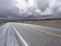 a lone, empty road stretches across the desert area, under stormy skies, and black clouds