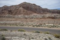 a motorcyclist rides on the road in an arid area near an mountain