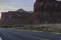 a lone long asphalt road passing past large canyons and towering rocks in the distance