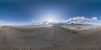 an empty road in the middle of nowhere with mountains in the background and clouds in the sky