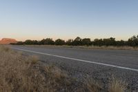 a long empty road with mountains in the distance with a car in the foreground