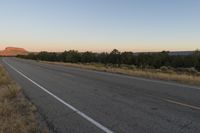 a long empty road with mountains in the distance with a car in the foreground